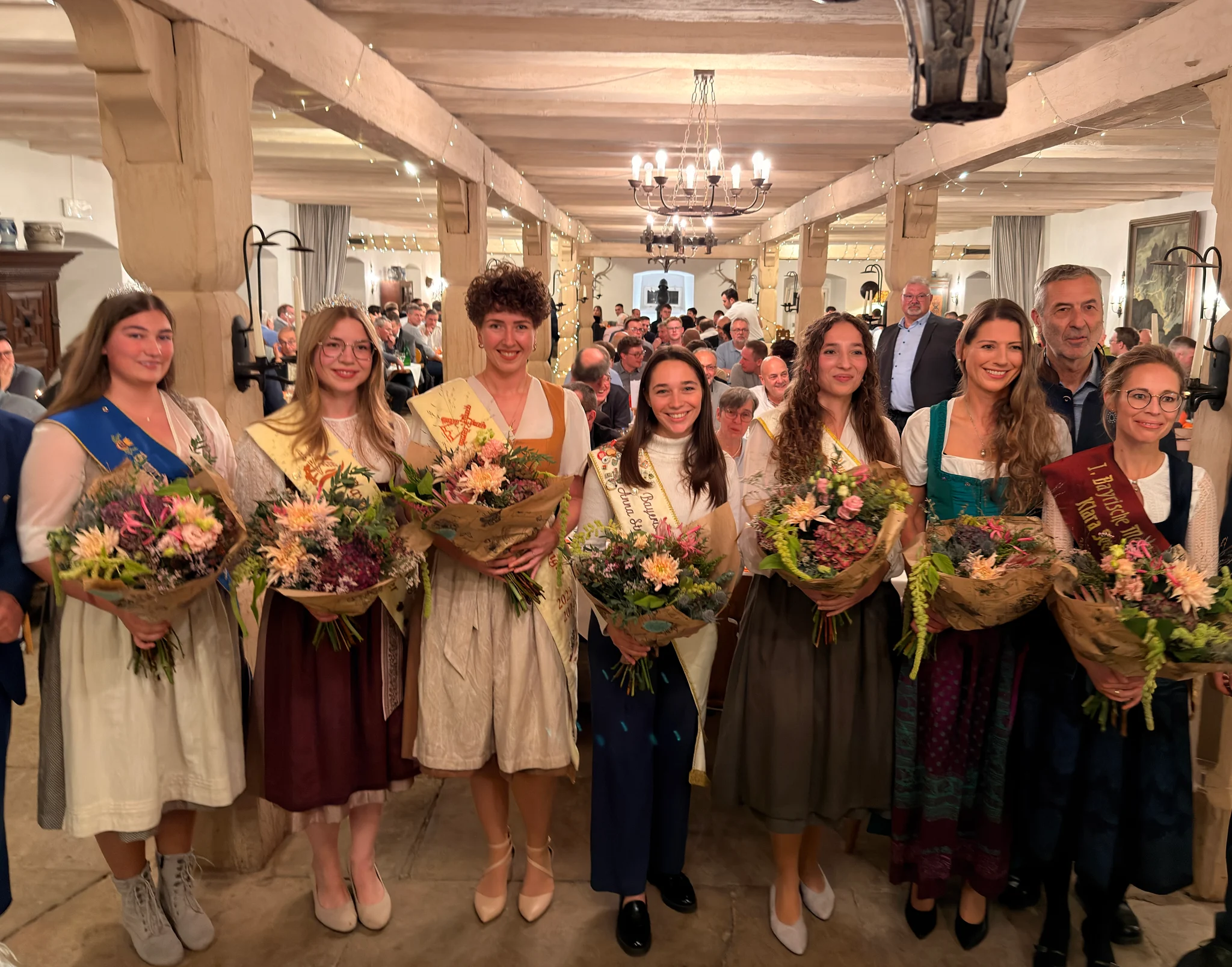 Die Mehlköniginnen mit Schärpen und Blumensträußen beim Fränkischen Abend im Schloss Sulzheim; dahinter sitzen Tagungsgäste an den Tischen